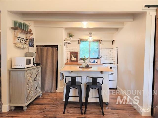 kitchen featuring a kitchen breakfast bar, dark hardwood / wood-style floors, white appliances, and beam ceiling