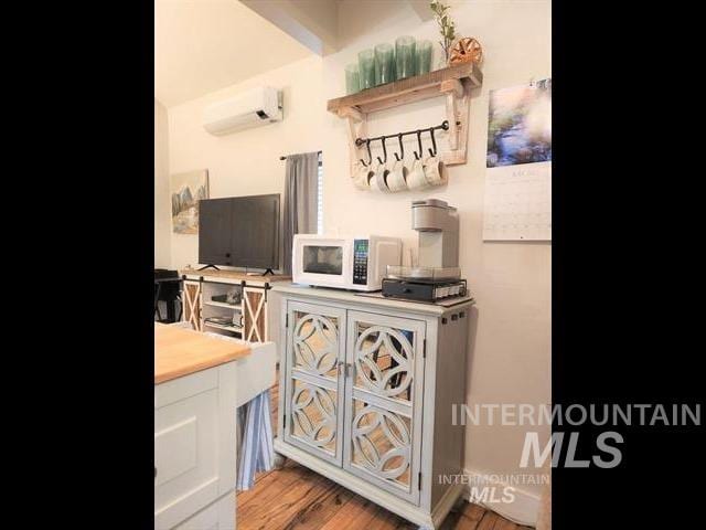 bar featuring a wall mounted air conditioner, hardwood / wood-style floors, and white cabinets