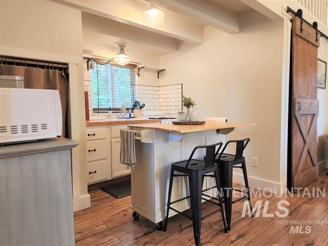 kitchen with a breakfast bar area, butcher block counters, white cabinetry, wood-type flooring, and a barn door