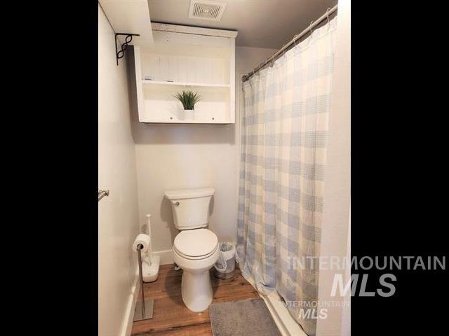 bathroom with hardwood / wood-style floors, toilet, and a shower with shower curtain