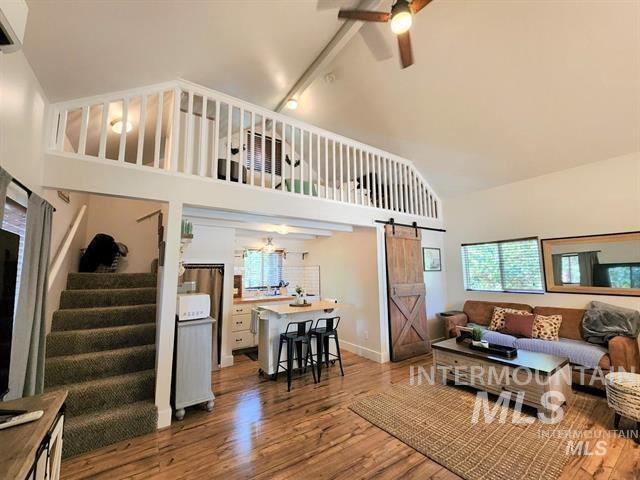 living room featuring hardwood / wood-style flooring, ceiling fan, a barn door, and high vaulted ceiling