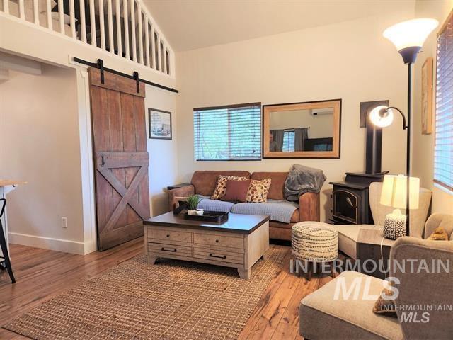 living room featuring wood-type flooring, a barn door, high vaulted ceiling, and a wood stove