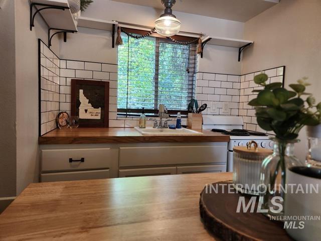 kitchen featuring white range, sink, decorative backsplash, and wooden counters