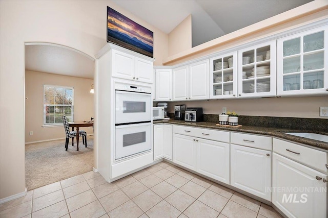 kitchen featuring lofted ceiling, light tile patterned floors, white cabinetry, dark stone counters, and white appliances