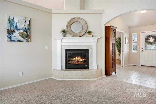 unfurnished living room featuring a tiled fireplace, vaulted ceiling, and light colored carpet