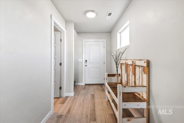 hall with baseboards, visible vents, and light wood-style floors