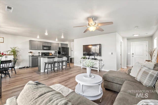 living room featuring light wood-type flooring, ceiling fan, visible vents, and baseboards