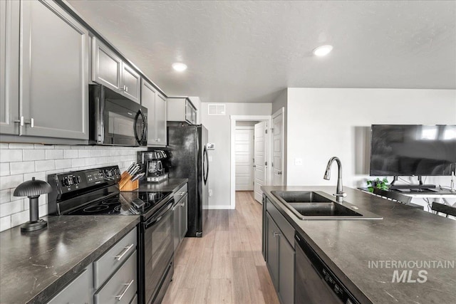 kitchen with visible vents, a sink, light wood-type flooring, black appliances, and backsplash