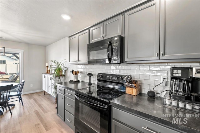 kitchen featuring decorative backsplash, light wood-style floors, dark countertops, gray cabinets, and black appliances