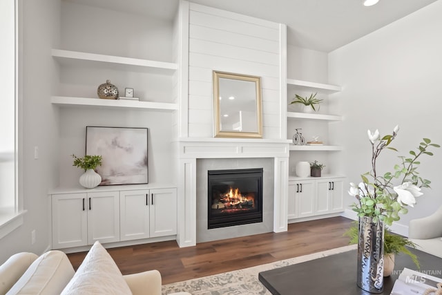 living room with a fireplace, built in shelves, and dark wood-style flooring