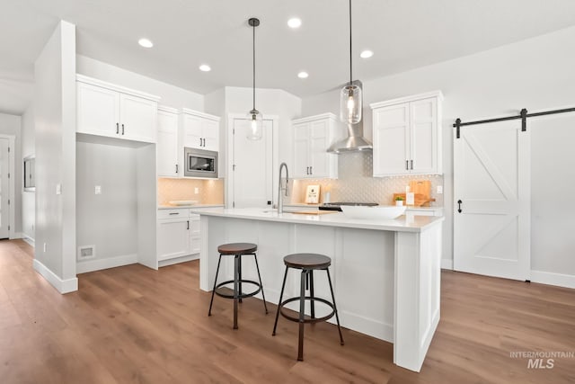 kitchen with a sink, light countertops, white cabinets, stainless steel microwave, and wall chimney exhaust hood
