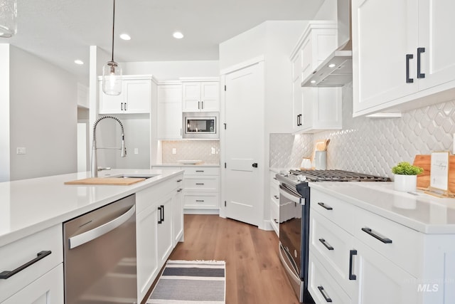 kitchen featuring wall chimney range hood, decorative light fixtures, light countertops, appliances with stainless steel finishes, and a sink
