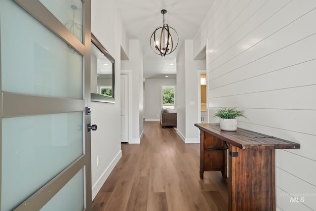 hall with an inviting chandelier, wood finished floors, and baseboards