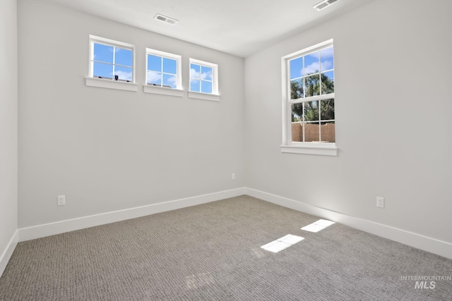 carpeted spare room featuring visible vents, baseboards, and a healthy amount of sunlight