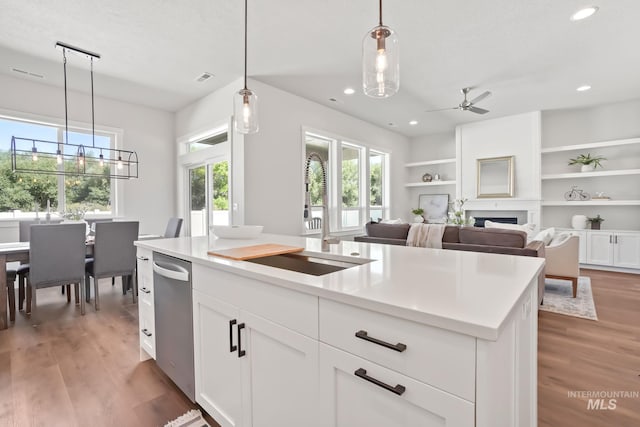 kitchen featuring a sink, decorative light fixtures, a fireplace, light wood finished floors, and ceiling fan