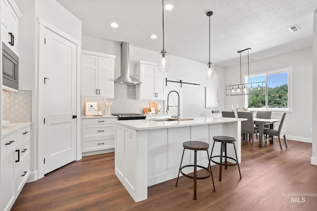 kitchen featuring light countertops, dark wood-style floors, white cabinetry, wall chimney exhaust hood, and a sink