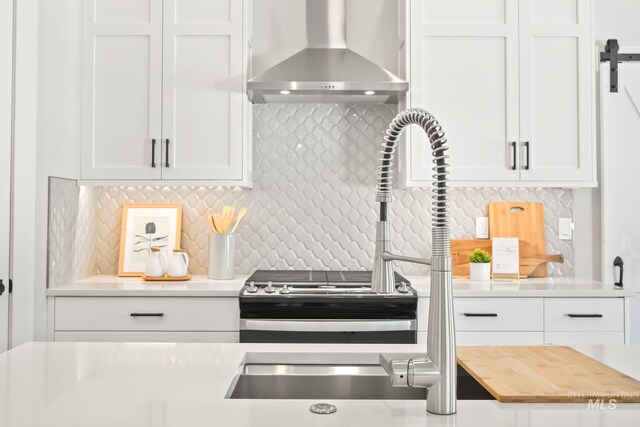 kitchen with decorative backsplash, white cabinetry, light countertops, and wall chimney range hood