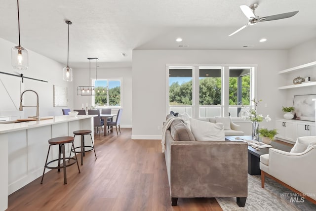 living area with recessed lighting, a ceiling fan, a barn door, and wood finished floors