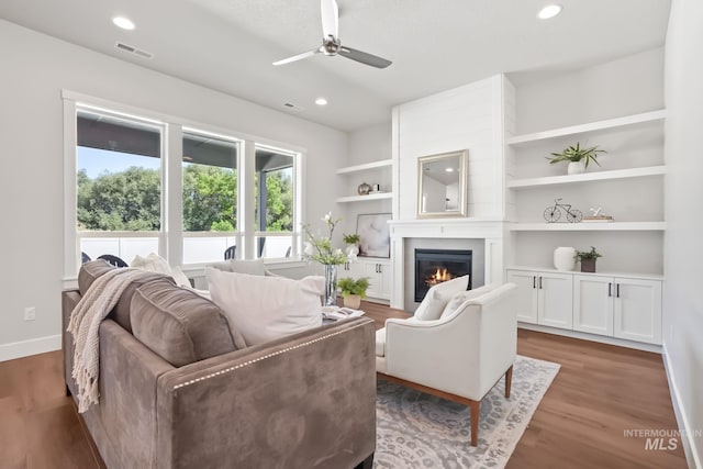 living area featuring built in shelves, wood finished floors, recessed lighting, a fireplace, and ceiling fan
