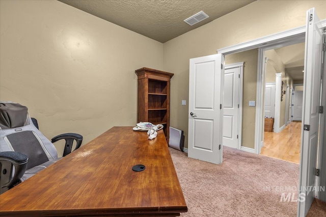 office space featuring a textured ceiling, visible vents, and light colored carpet