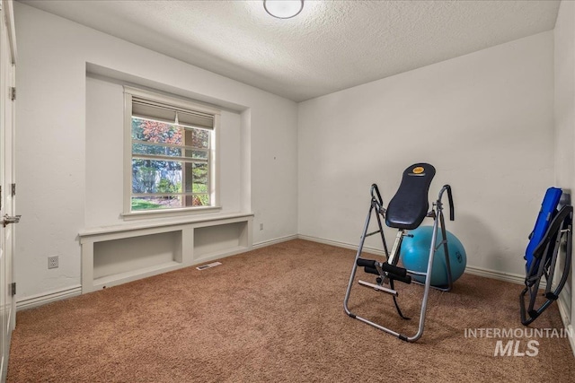 workout area with a textured ceiling, baseboards, visible vents, and carpet