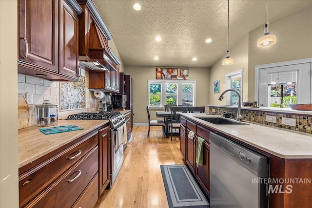 kitchen with hanging light fixtures, a sink, decorative backsplash, light wood-style floors, and appliances with stainless steel finishes
