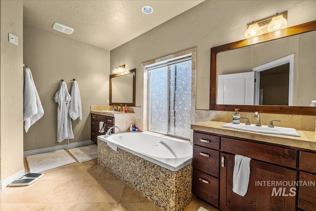 bathroom featuring a garden tub, a textured ceiling, two vanities, and a sink