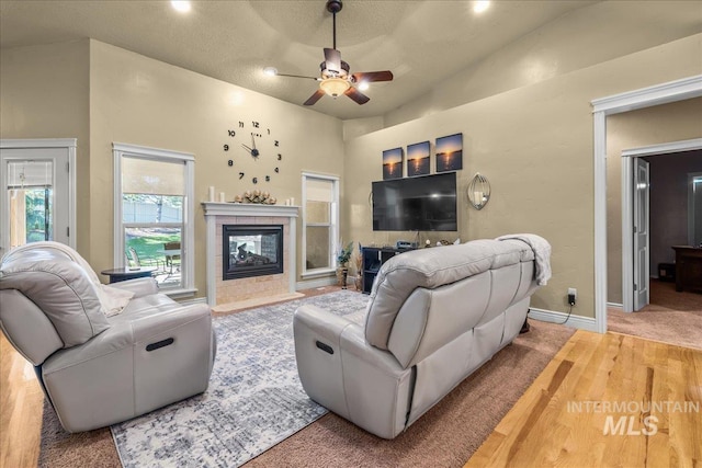 living room with a ceiling fan, baseboards, a tiled fireplace, and wood finished floors
