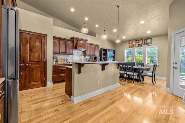 kitchen with freestanding refrigerator, recessed lighting, a textured ceiling, a kitchen breakfast bar, and light countertops