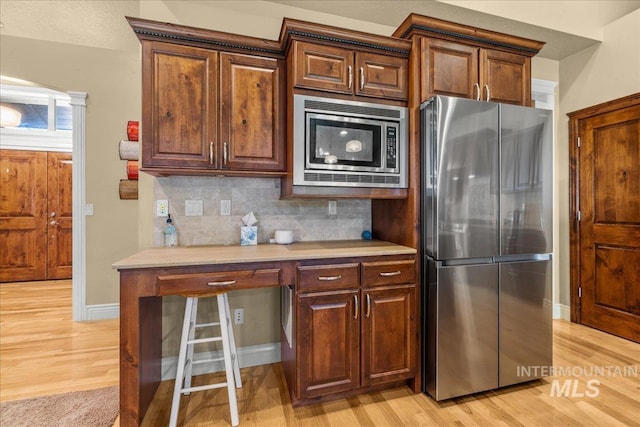 kitchen featuring light wood finished floors, tasteful backsplash, and appliances with stainless steel finishes