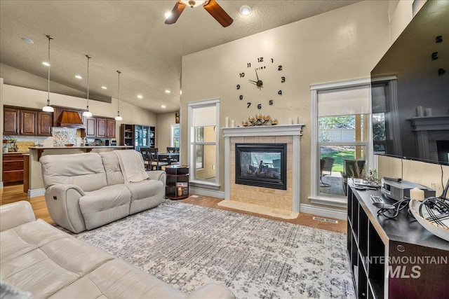 living area with ceiling fan, a wealth of natural light, and a tiled fireplace