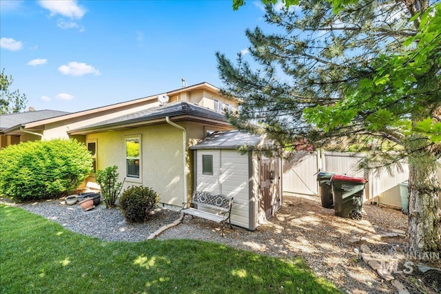 back of property featuring stucco siding, fence, an outbuilding, and a shed
