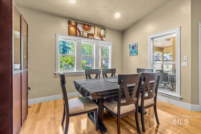 dining space featuring baseboards, light wood finished floors, and a textured ceiling