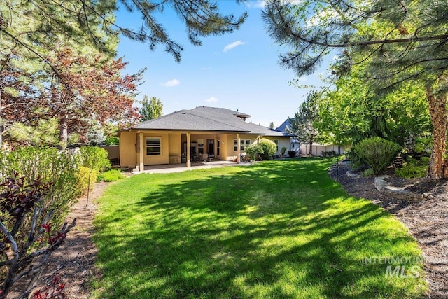 rear view of property with a yard, a patio, stucco siding, and fence