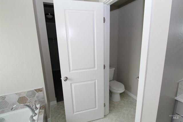 bathroom featuring a washtub, toilet, and baseboards