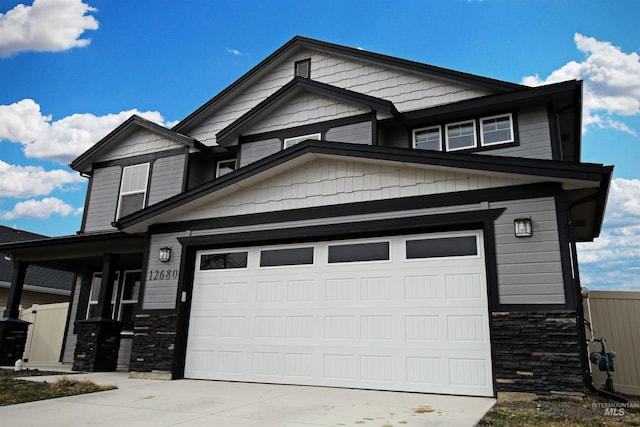 craftsman-style home featuring stone siding, fence, concrete driveway, and an attached garage