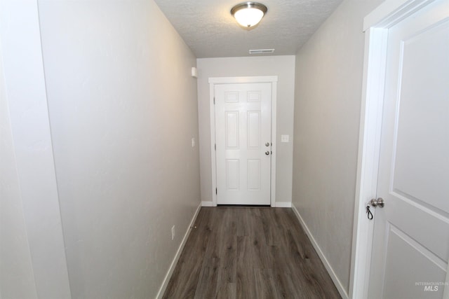 hallway with a textured ceiling, wood finished floors, visible vents, and baseboards