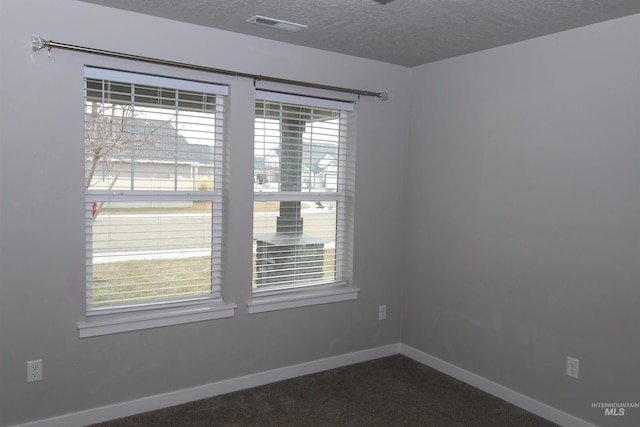 spare room featuring baseboards, visible vents, dark colored carpet, and a textured ceiling