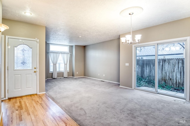 foyer entrance featuring light carpet, a textured ceiling, and an inviting chandelier