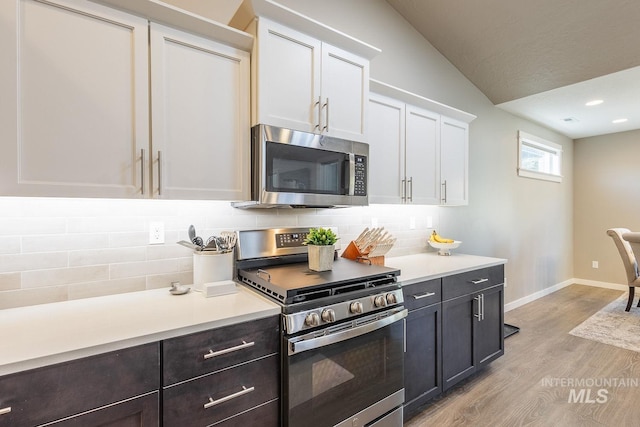 kitchen with white cabinets, appliances with stainless steel finishes, lofted ceiling, decorative backsplash, and light hardwood / wood-style flooring