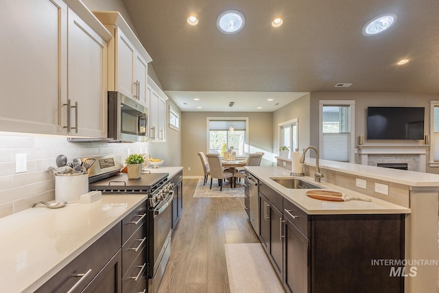 kitchen with white cabinets, appliances with stainless steel finishes, an island with sink, light hardwood / wood-style floors, and sink