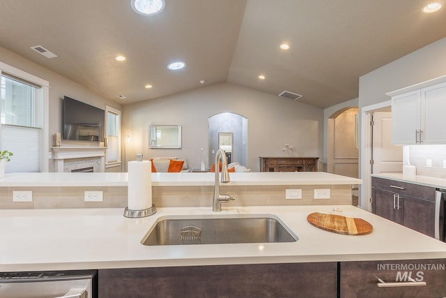 kitchen featuring lofted ceiling, stainless steel dishwasher, sink, dark brown cabinetry, and an island with sink