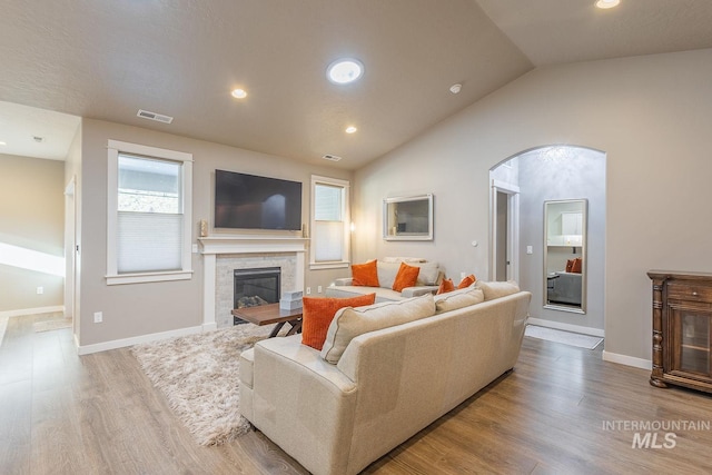 living room with light wood-type flooring, vaulted ceiling, and a tile fireplace