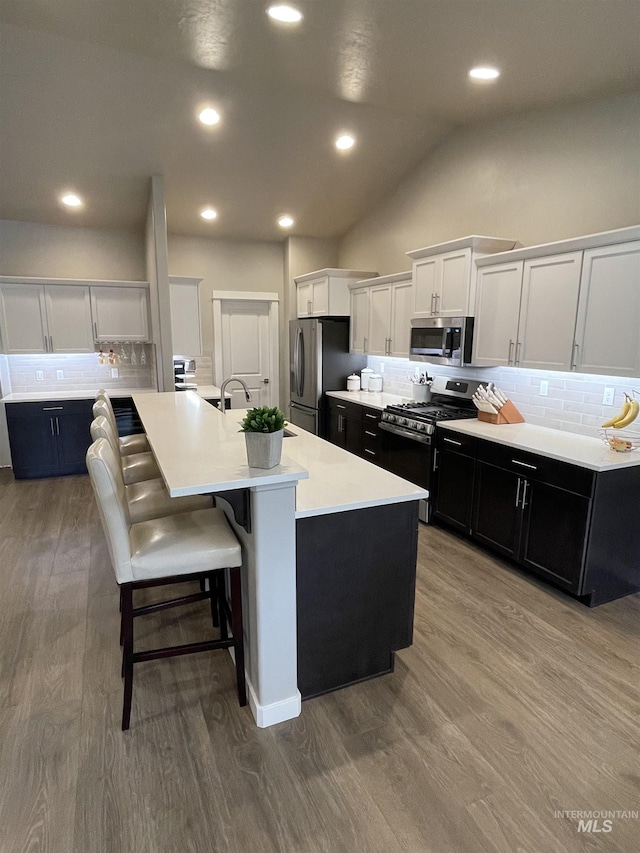 kitchen with white cabinetry, appliances with stainless steel finishes, decorative backsplash, a kitchen island with sink, and a kitchen breakfast bar