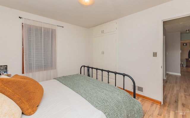 bedroom with light wood finished floors, visible vents, and baseboards