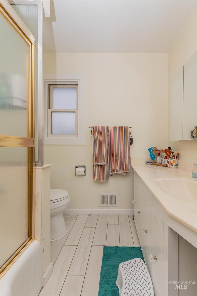 full bathroom featuring visible vents, baseboards, combined bath / shower with glass door, toilet, and vanity