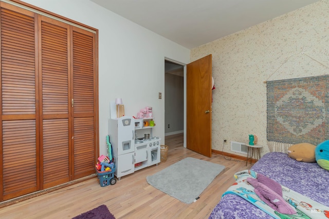 bedroom featuring a closet, visible vents, wood finished floors, wallpapered walls, and baseboards