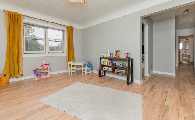 rec room featuring baseboards, a textured ceiling, and hardwood / wood-style floors