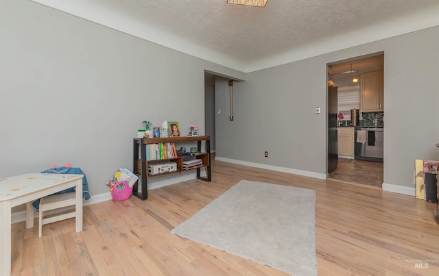 interior space with light wood finished floors, baseboards, and a textured ceiling