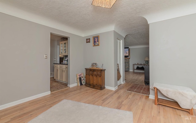 corridor with baseboards, light wood-style floors, and a textured ceiling